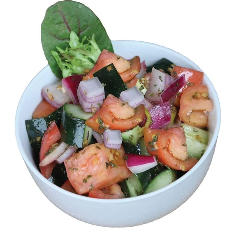 A white bowl filled with a fresh salad of chopped tomatoes, cucumbers, and red onions.