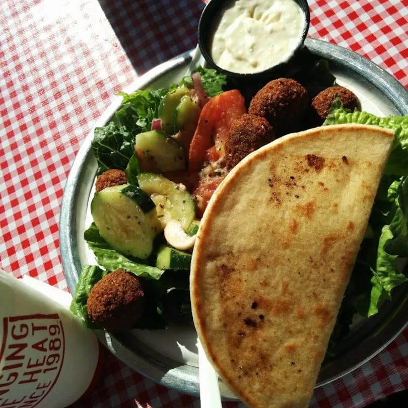Gyro Wrap falafel plate with pita bread, salad, and a side of tzatziki sauce on a red checkered tablecloth.
